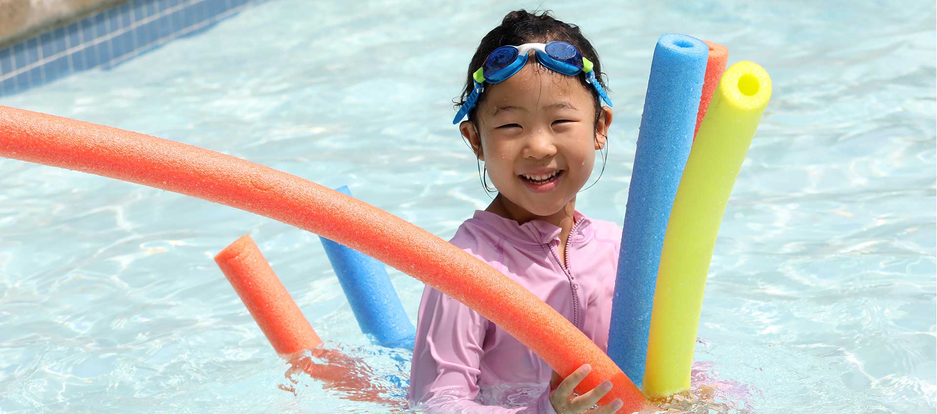 A camper in the pool with colorful pool noodles